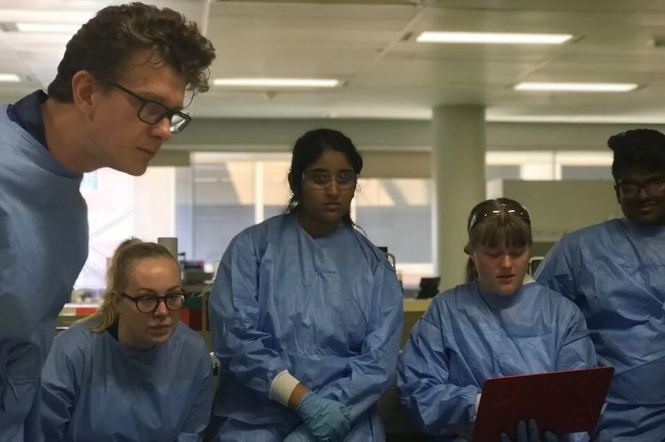 People in lab coats examining a tablet.