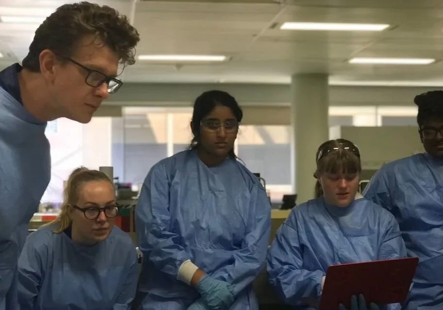 People in lab coats examining a tablet.